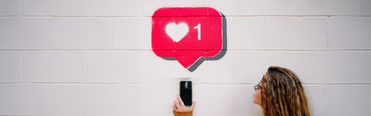 girl-holding-a-phone-with-a-like-symbol-painted-on-the-wall